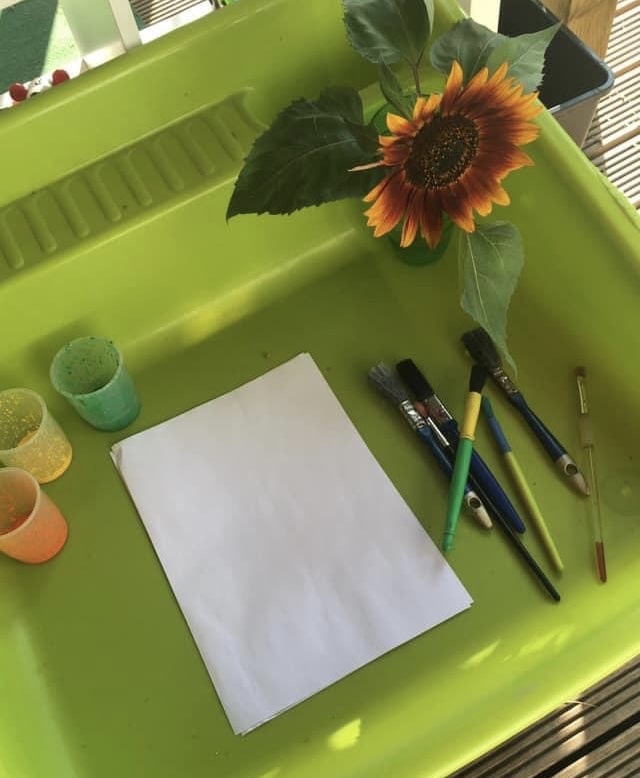 Workspace containing paper, brushes, paint and a sunflower