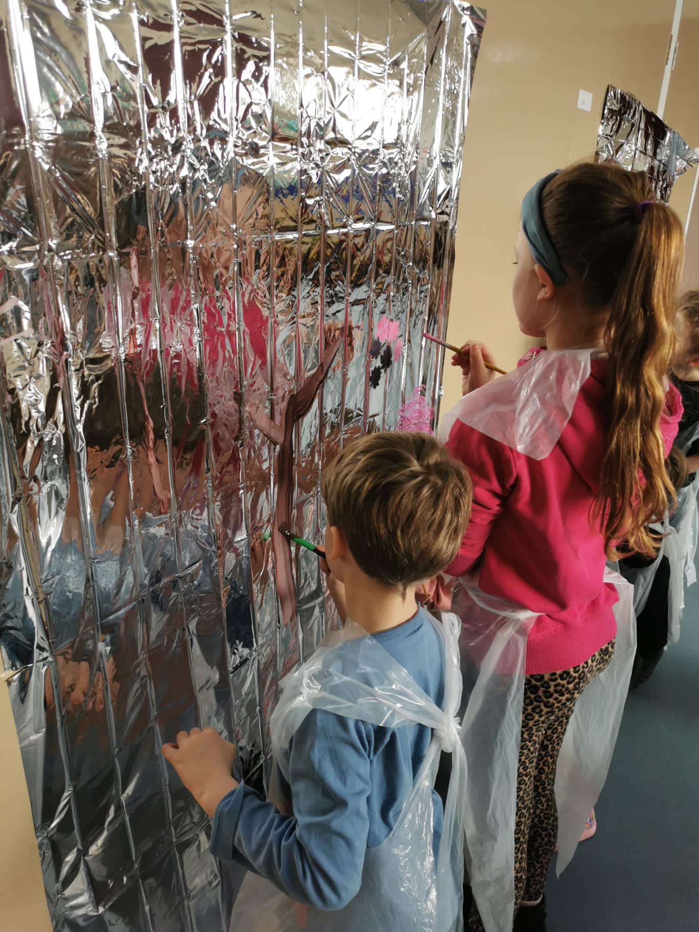 A boy and girl painting on silver foil hanging on a wall